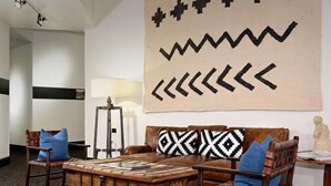 A cozy room with a brown leather sofa, two wooden chairs, a wooden coffee table, and a large wall hanging with geometric patterns. - Independence Square Unit 309 | Downtown Hotel Room with A/C in Aspen, Wet Bar & More (Aspen)