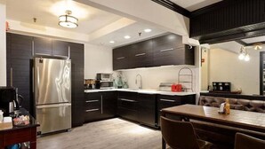A modern kitchen with dark cabinetry, stainless steel appliances, and a dining area with a wooden table and leather seating. - Independence Square Unit 309 | Downtown Hotel Room with A/C in Aspen, Wet Bar & More (Aspen)