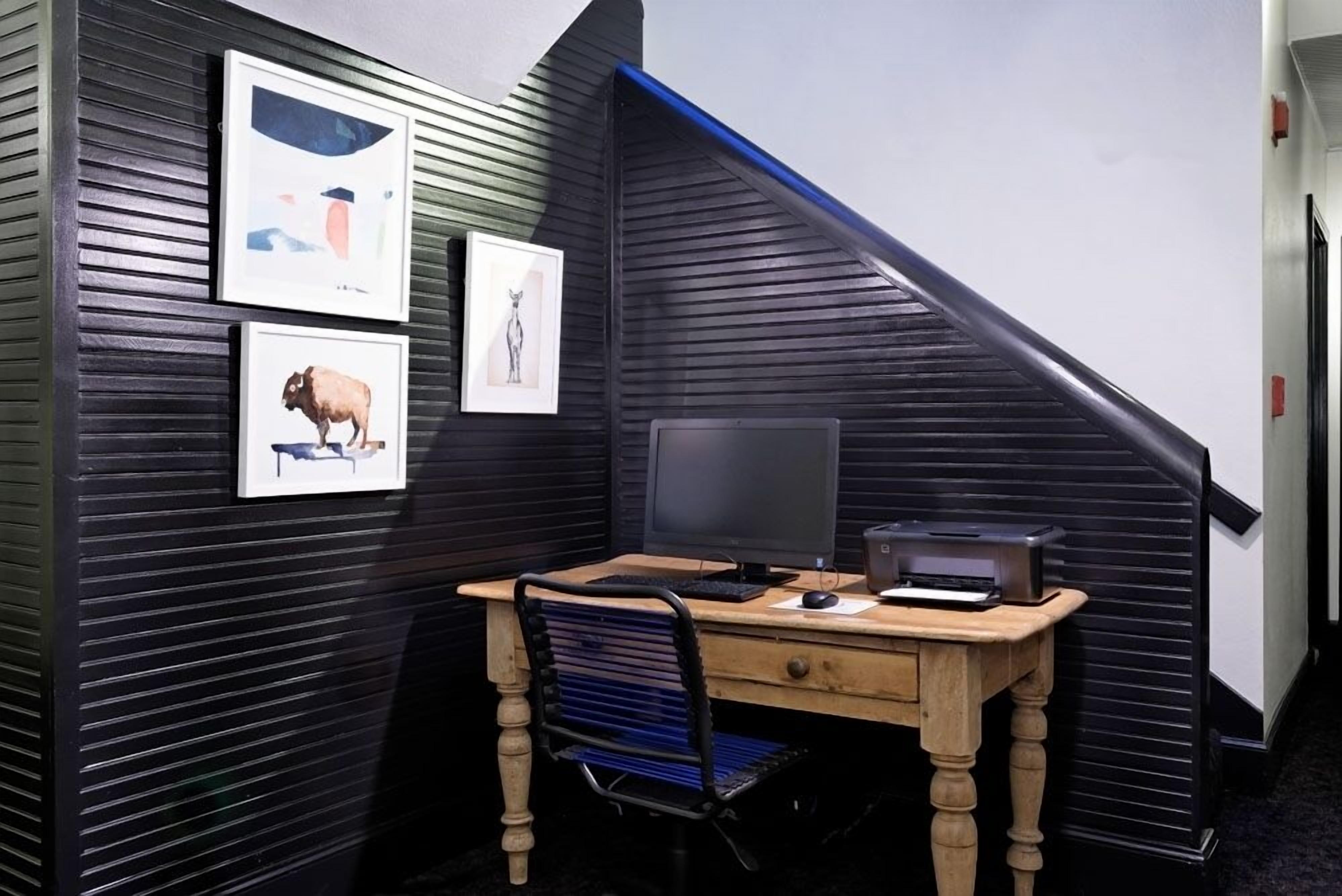 A corner office with a desk, computer, and chair. There are framed pictures on the wall.