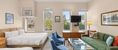 A hotel room with two beds, a sofa, a TV, and a desk.