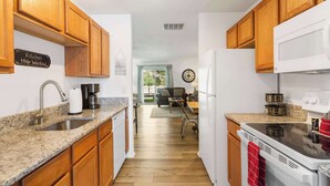 A kitchen with wooden cabinets, a granite countertop, a sink, a stove, and a dining area with a table and chairs. - Rustic Retreat Your Own Private Retreat in the Heart of Branson! (Branson)