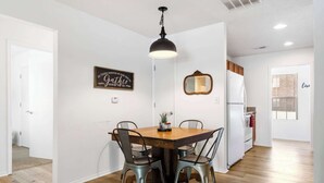 A dining area with a wooden table and four chairs, a pendant light, a wall-mounted mirror, and a refrigerator in the background. - Rustic Retreat Your Own Private Retreat in the Heart of Branson! (Branson)