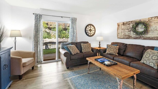 A living room with a brown leather sofa, a wooden coffee table, a blue rug, and a large wall clock. - Rustic Retreat Your Own Private Retreat in the Heart of Branson! (Branson)