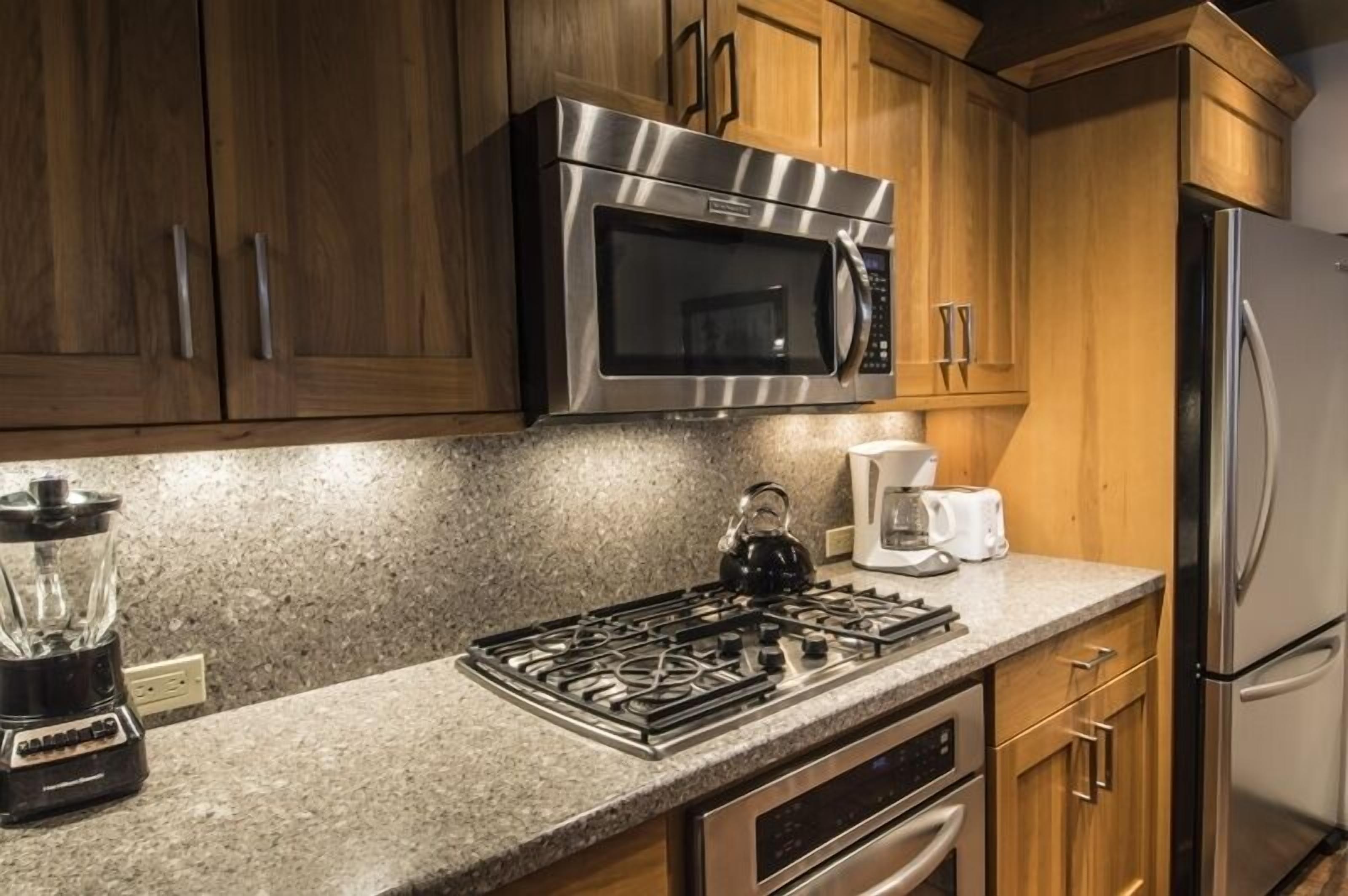A kitchen with wooden cabinets, a stainless steel microwave, a gas stove, a coffee maker, and a refrigerator.