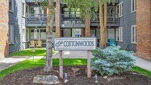 Un letrero para The Cottonwoods, un edificio de apartamentos de varios pisos con balcones, un pequeño césped y un árbol en primer plano.