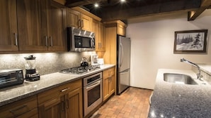 Una cocina con gabinetes de madera, microondas de acero inoxidable, estufa a gas, refrigerador y encimera de granito.