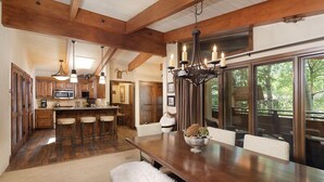 A spacious kitchen with wooden beams, a central island with stools, a chandelier, and large windows offering a view of the outdoors. - Little Nell Condominiums Unit 11 | Top Floor Condo with Mountain Views, 3 Blocks to Gondola (Aspen)