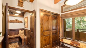 A wooden bench with a cushioned seat, a wooden door, and a window with a view of greenery. - Little Nell Condominiums Unit 11 | Top Floor Condo with Mountain Views, 3 Blocks to Gondola (Aspen)