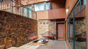 A stone-walled outdoor patio with a wooden deck, a bench, and a table. - Fasching Haus Unit 12 | Lower Level Deluxe Condo w/ Open Living Area & Gas Fireplace (Aspen)