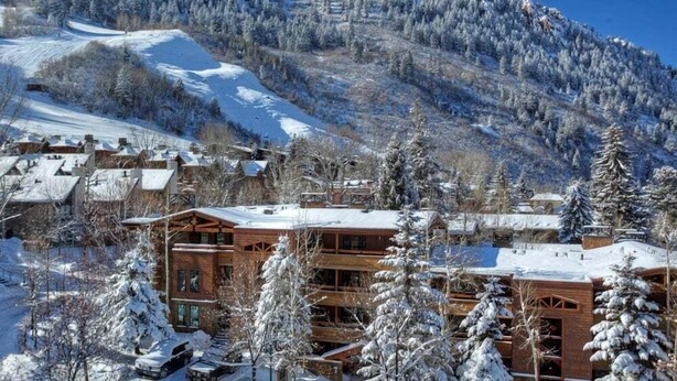 A snow-covered lodge with multiple floors, surrounded by snow-laden trees and a mountainous backdrop. - Fasching Haus Unit 12 | Lower Level Deluxe Condo w/ Open Living Area & Gas Fireplace (Aspen)