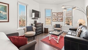 A modern living room with a fireplace, comfortable seating, and large windows offering a view of the city. - Independence Square Unit 303 | Corner Studio with Premier Finishes, Downtown Location (Aspen)