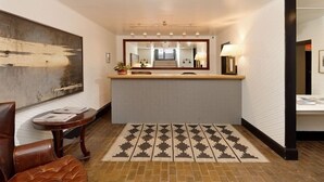 A hotel lobby with a reception desk, a large abstract painting, a patterned rug, and a leather chair. - Independence Square Unit 303 | Corner Studio with Premier Finishes, Downtown Location (Aspen)