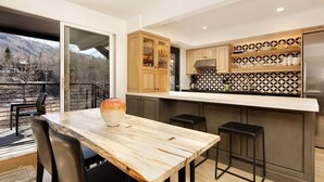 Eine moderne Küche mit einer Holzinsel, Barhocker und Bergblick durch eine Schiebetür.