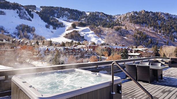 Ein Whirlpool auf einer Holzterrasse mit Blick auf einen verschneiten Berg und eine Wohngegend.