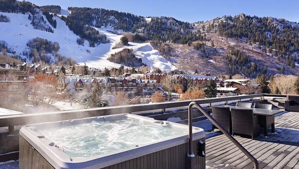 Un jacuzzi en una terraza de madera con vista a una montaña nevada y una zona residencial.