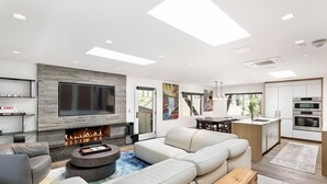 A modern living room with a fireplace, a large flat-screen TV, a sectional sofa, and a dining area.