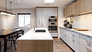 A modern kitchen with a central island, built-in appliances, and a dining area with a long table and chairs.