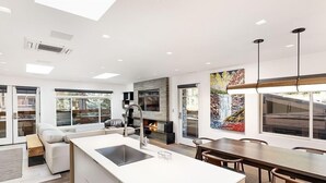 A modern kitchen with a central island, a dining area with a wooden table, and a fireplace.
