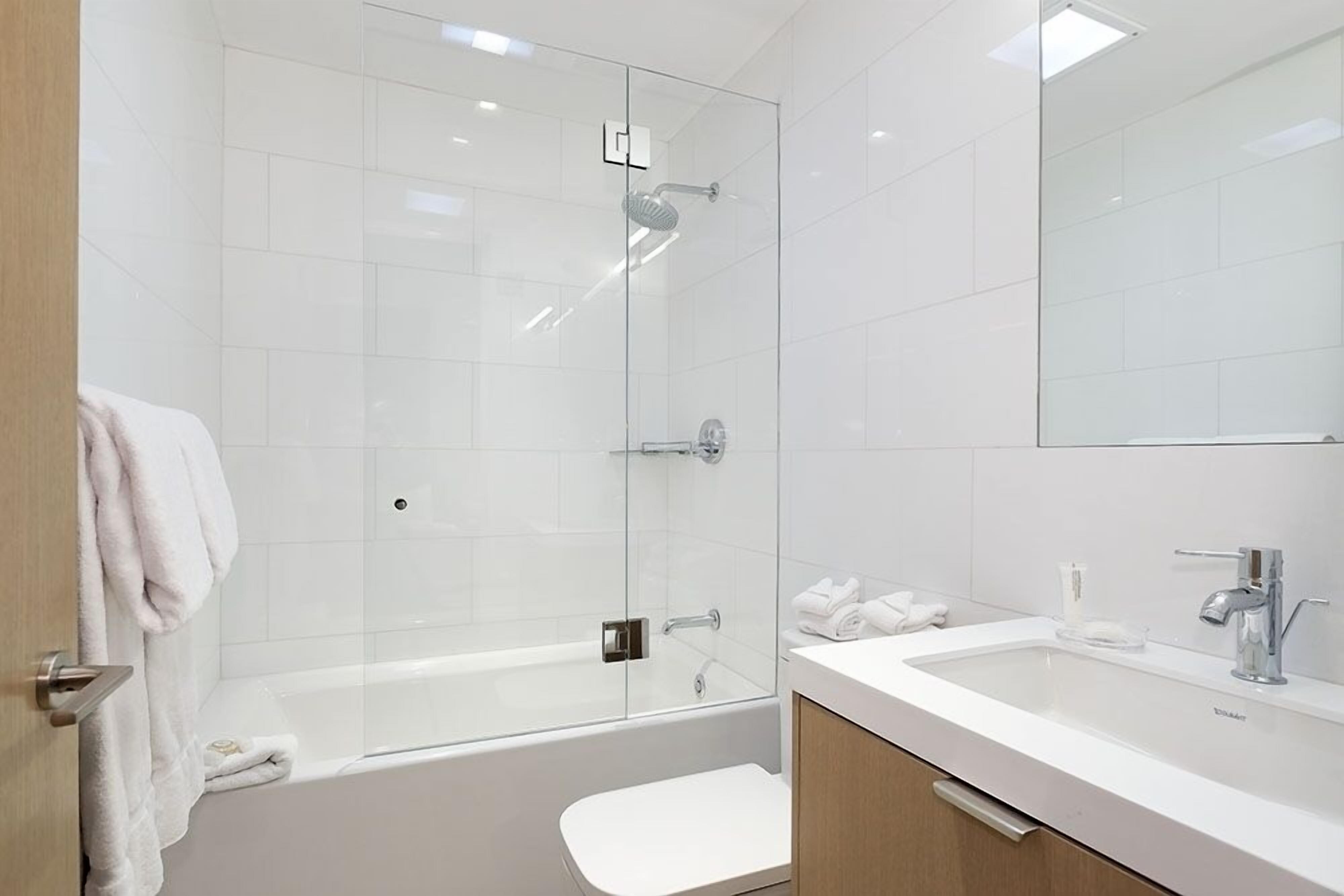 A modern bathroom with a glass-enclosed shower, a white bathtub, and a vanity with a sink and mirror.