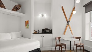 Una habitación de hotel con cama, una kitchenette pequeña, un comedor con dos sillas y una mesa, y una decoración de pared temática de esquí.