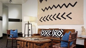 A modern living room with a brown leather sofa, blue cushions, a wooden coffee table, and a large wall art piece. - Independence Square 211 | Chic Hotel Room with Mountain Views, A/C, & Rooftop Hot Tub (Aspen)