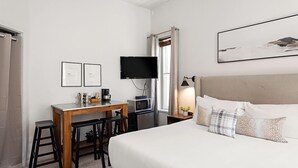 A hotel room with a bed, a desk with a computer, a TV, and a window with curtains. - Independence Square 211 | Chic Hotel Room with Mountain Views, A/C, & Rooftop Hot Tub (Aspen)