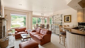 A spacious living room with a fireplace, leather sofas, a dining area, and a kitchen with a bar.