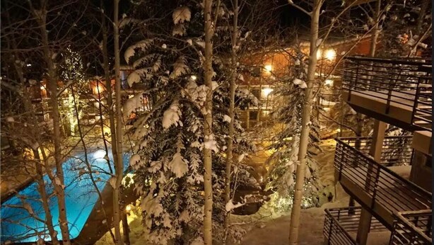 Un espace extérieur enneigé comprenant une piscine, des arbres et un bâtiment doté de balcons.