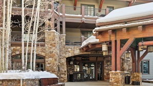 A multi-story building with stone walls, wooden balconies, and a covered entrance area. - The Ritz-Carlton | Three-Bedroom Premier Residence 8103, Ski-in & Ski-out Resort in Aspen Highlands (Aspen)