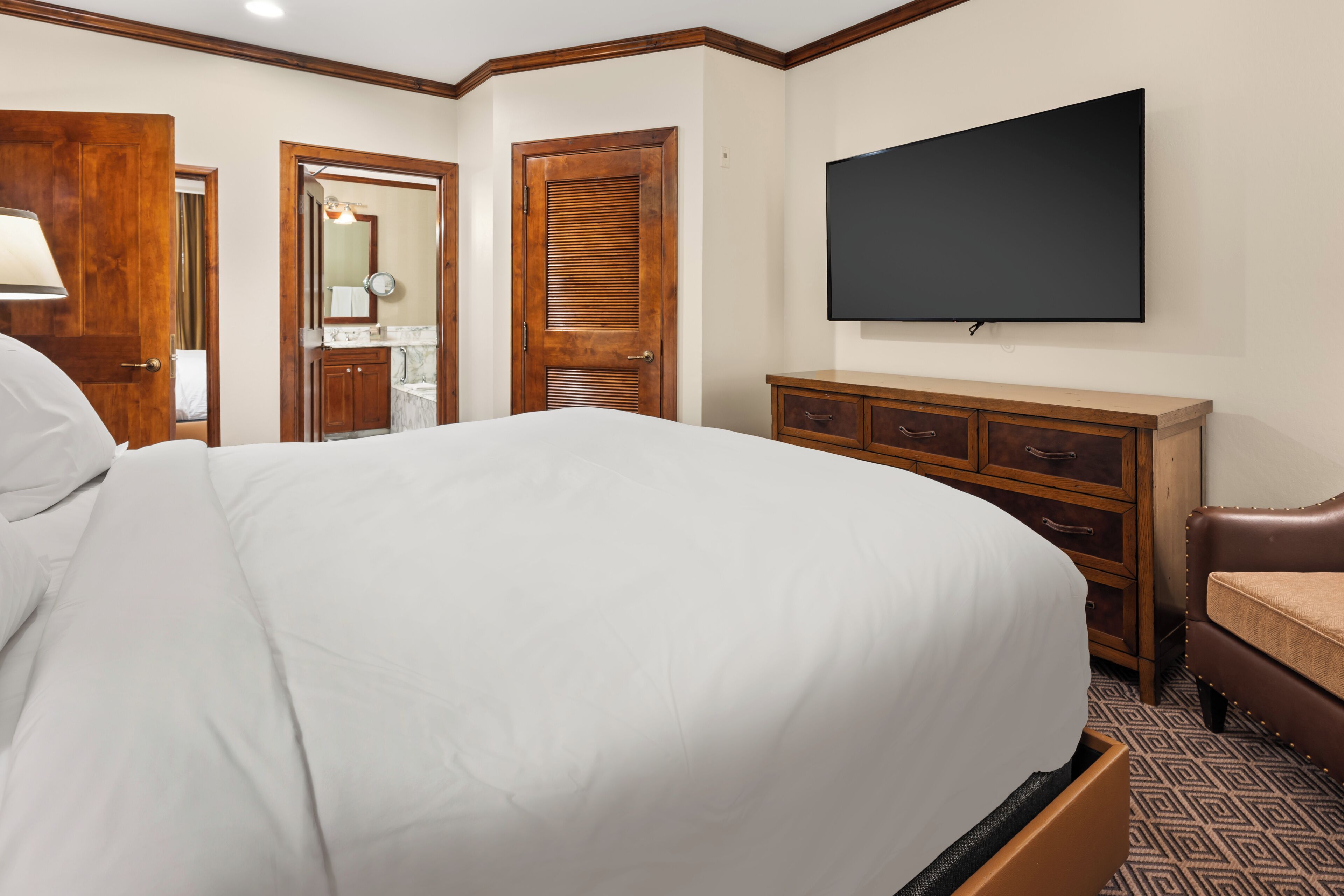 A hotel room with a large bed, wooden wardrobe, a flat-screen TV, and a bathroom visible through an open door.