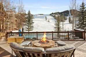 Une terrasse avec un foyer extérieur, des sièges et une vue sur une montagne enneigée.