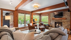 Una sala de estar acogedora con chimenea, muebles de cuero y ventanas amplias que ofrecen vistas al exterior.
