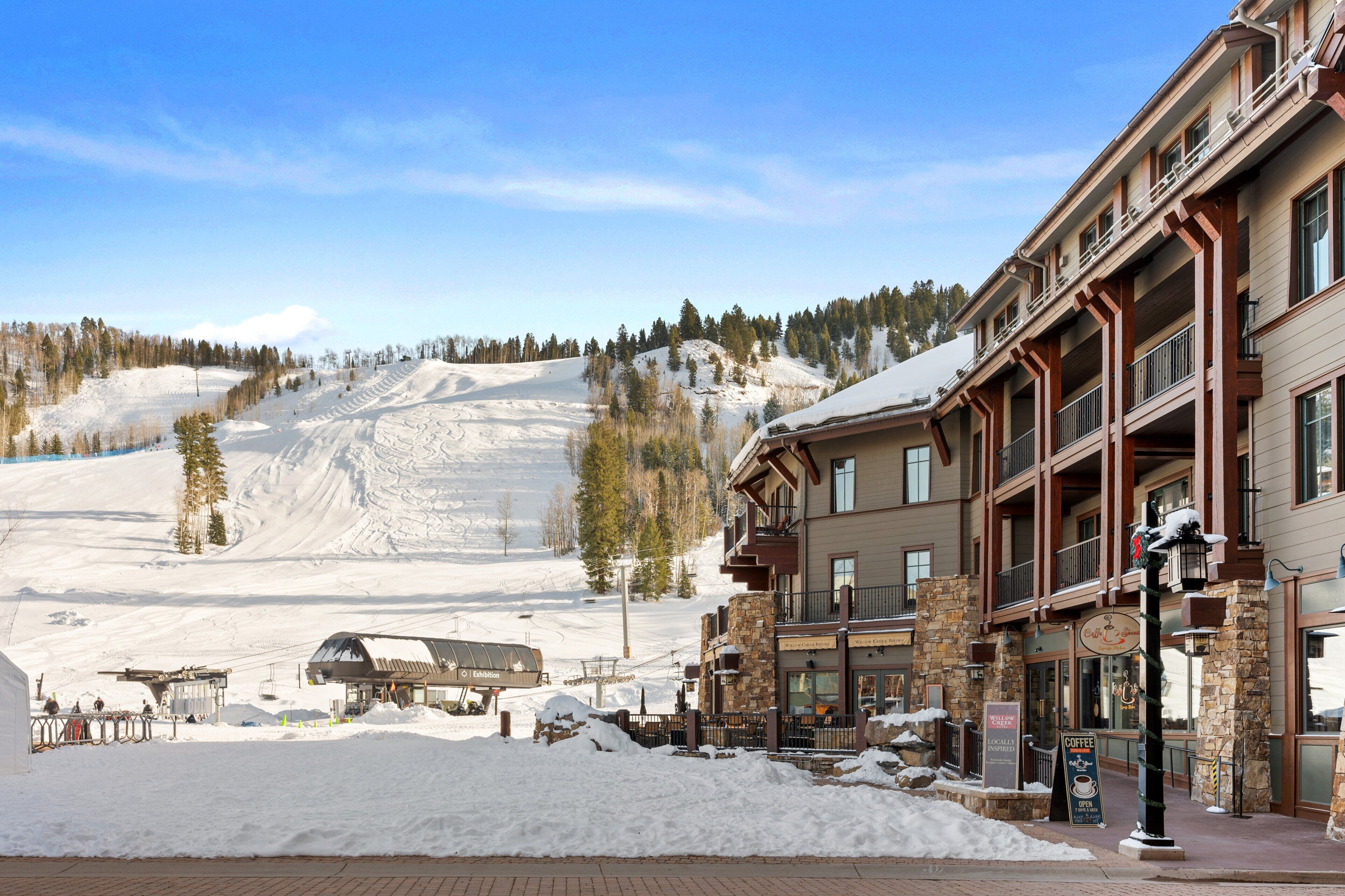 Un hôtel avec une piste de ski en arrière-plan, des piliers en pierre et une enseigne.