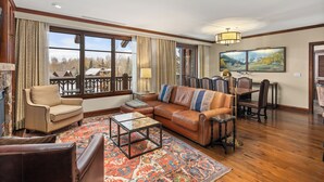A spacious living room with a large window, a leather sofa, a coffee table, and a dining area with a table and chairs. - The Ritz-Carlton | 3BR Residence 2310: Ski-in/Ski-out Resort in Aspen w/ Mountain/Town view (Aspen)