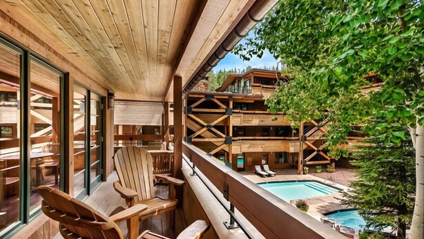 Un balcone in legno con vista sulla piscina, arredi in legno e cielo sereno.