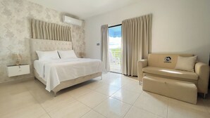 A bedroom with a bed, a nightstand, a sofa, a window with curtains, and an air conditioning unit. - MB Apartment A (Puerto Plata)
