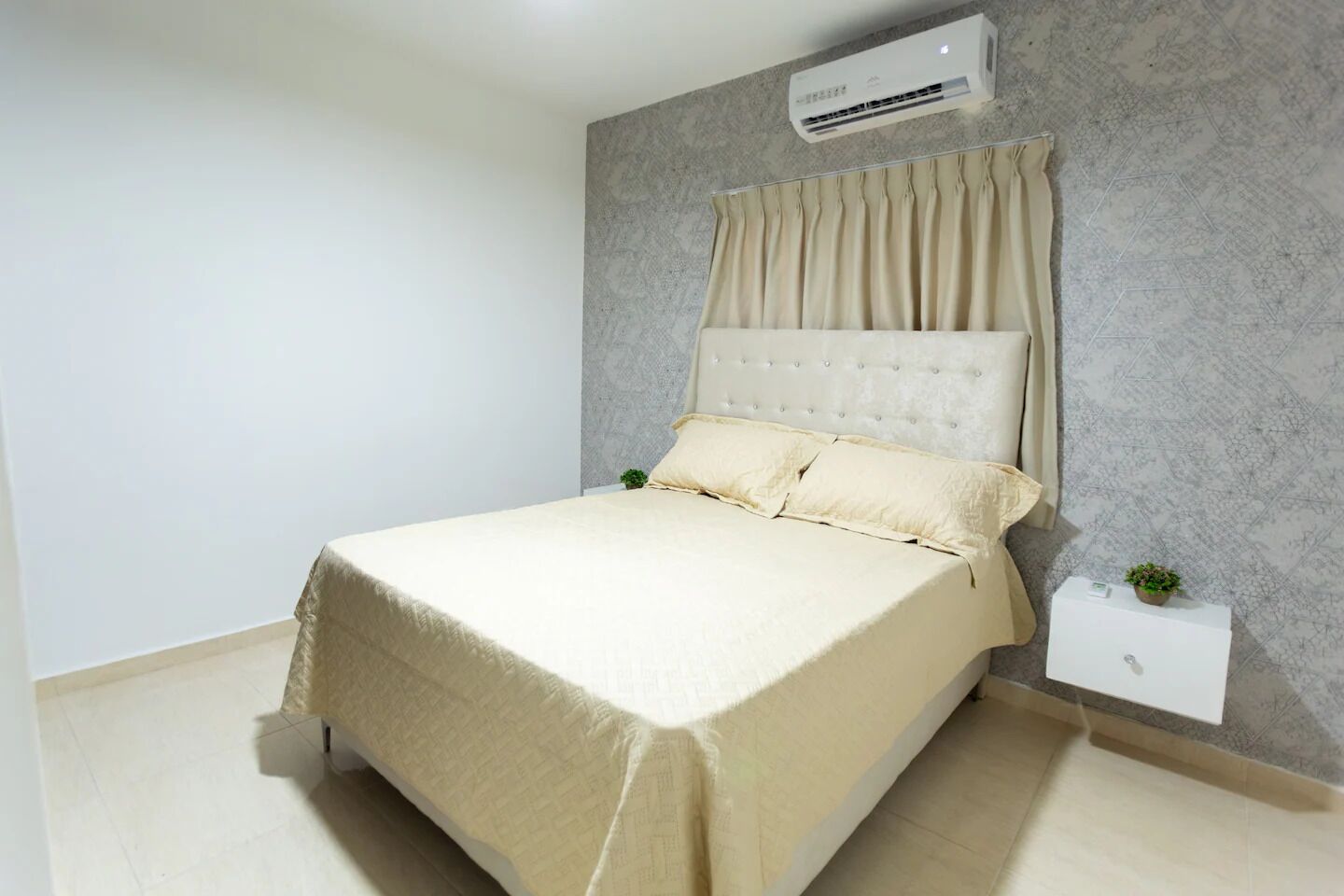 Een slaapkamer met een bed, een airconditioner, een nachtkastje en een kleine plant.
