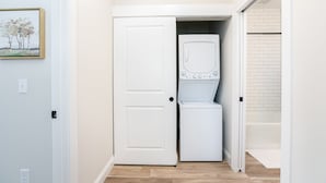 A laundry room with a washer and dryer, a white door, and a small painting on the wall. - Victory Views Estate: Luxury Guest Loft (South Bend)