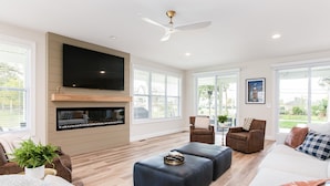 A modern living room with a flat-screen TV, fireplace, and large windows. - Victory Views Main House: Luxury Home for 20 Ppl (South Bend)