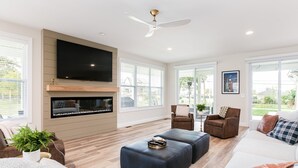 A modern living room with a flat-screen TV, fireplace, and large windows.