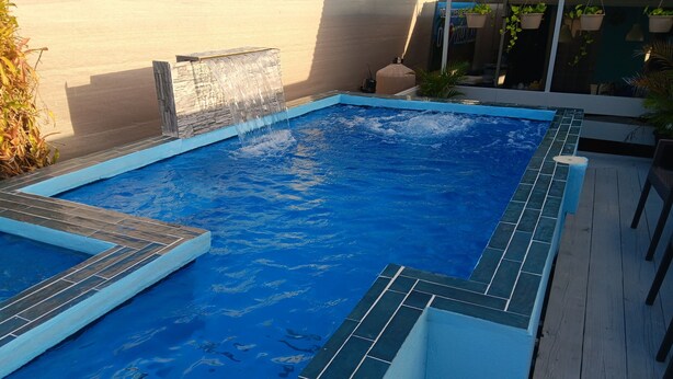 Ein Pool mit Wasserfall, umgeben von einer Holzterrasse und einer Steinmauer.