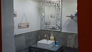 Ein Badezimmer mit einem weißen Waschbecken, dunklen Marmorfliesen, einem Zier-Spiegel und einer Deckenleuchte.
