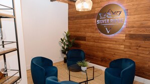 A modern lounge area with wooden paneling, a sign reading "Silver Ridge Ranch," and three blue chairs around a small table with a plant. - Silver Ridge Ranch (Easton)
