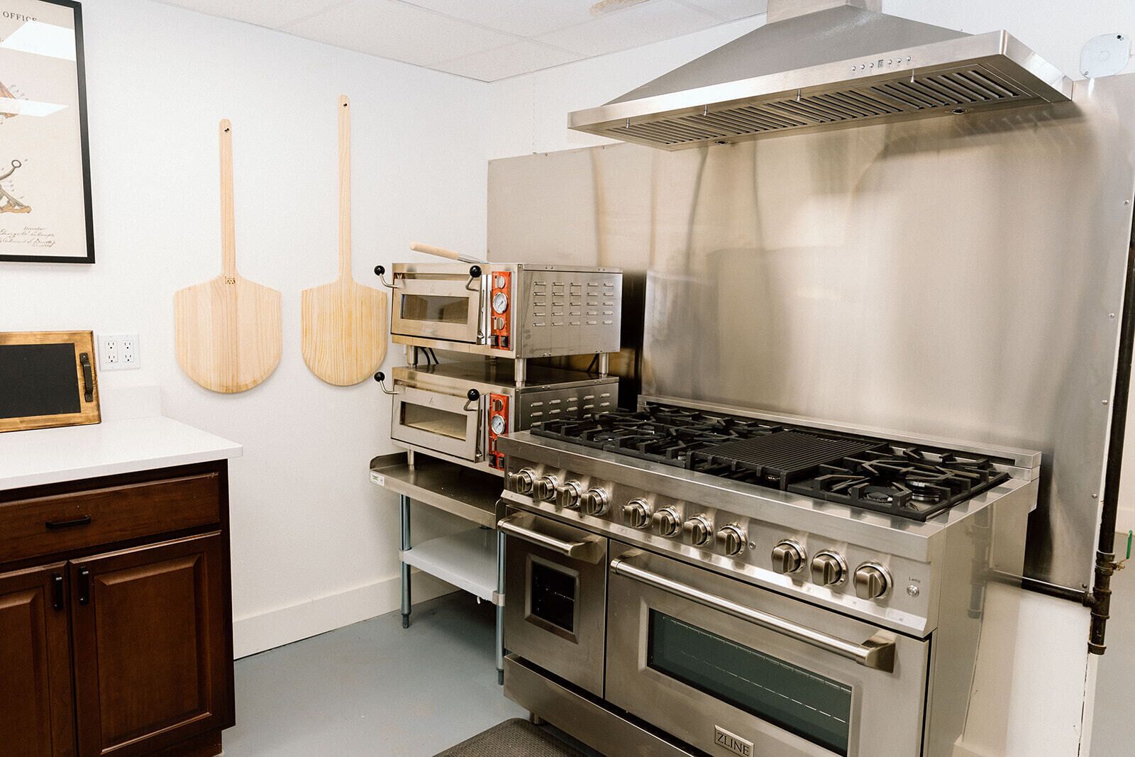 A commercial kitchen with stainless steel appliances, including a stove, ovens, and a pizza oven.