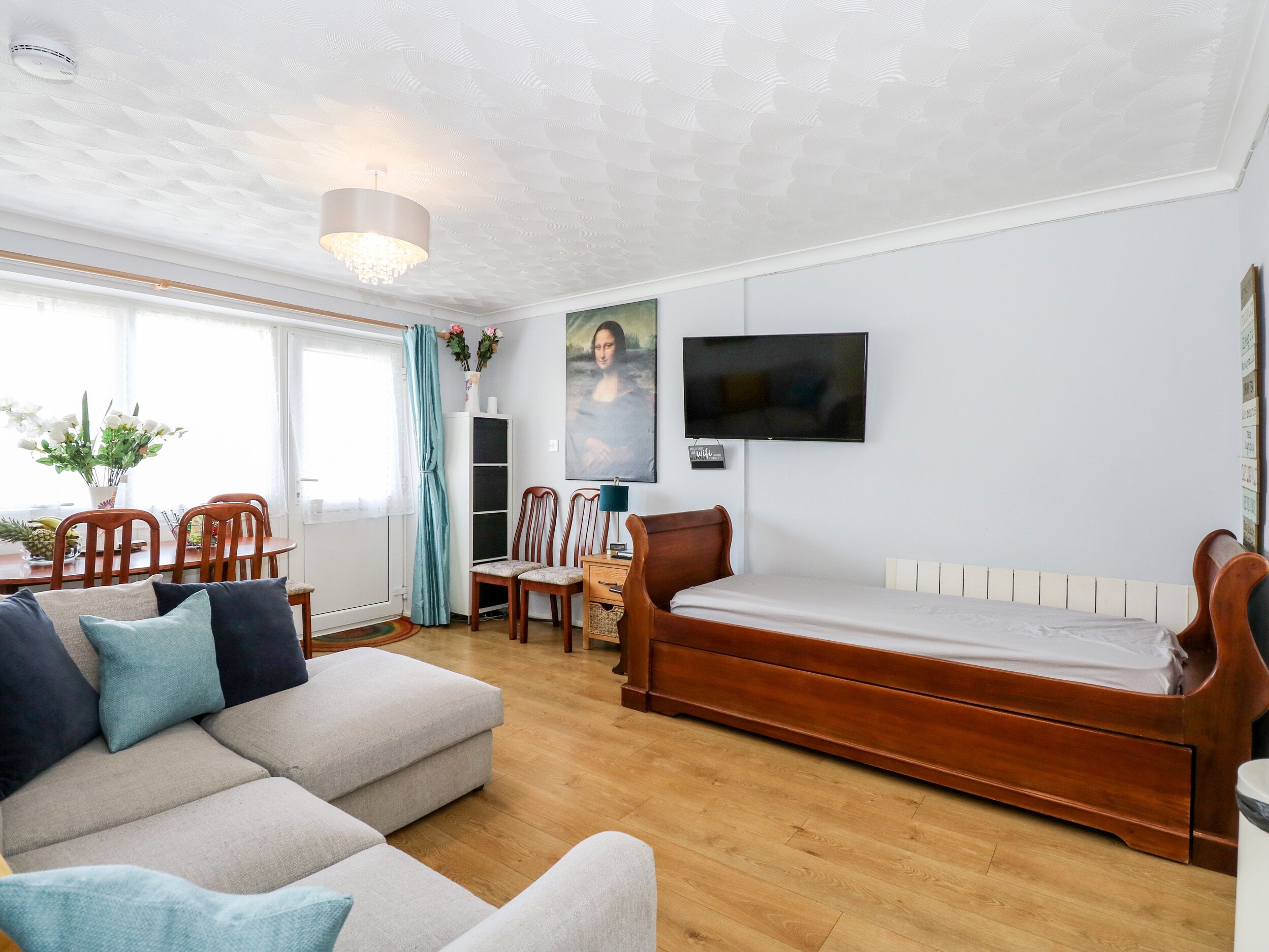 Un salon moderne comprenant un canapé, un lit en bois, une table à manger avec des chaises et un téléviseur fixé au mur.