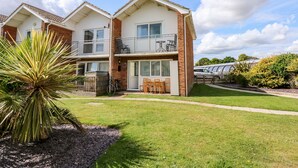 A two-story residential building with a balcony on the upper floor, a patio with outdoor furniture, and a well-maintained lawn. - 63 The Waterside Holiday Park (Lowestoft)