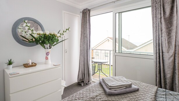 A bedroom with a bed, a dresser, a mirror, and a window with curtains. - 63 The Waterside Holiday Park (Lowestoft)