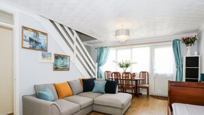 A living room with a grey sectional sofa, wooden dining table, and chairs. There is a staircase with white railings leading to another level. - 63 The Waterside Holiday Park (Lowestoft)