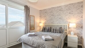 A neatly arranged bedroom with a bed, bedside tables, and a window with curtains. - 63 The Waterside Holiday Park (Lowestoft)