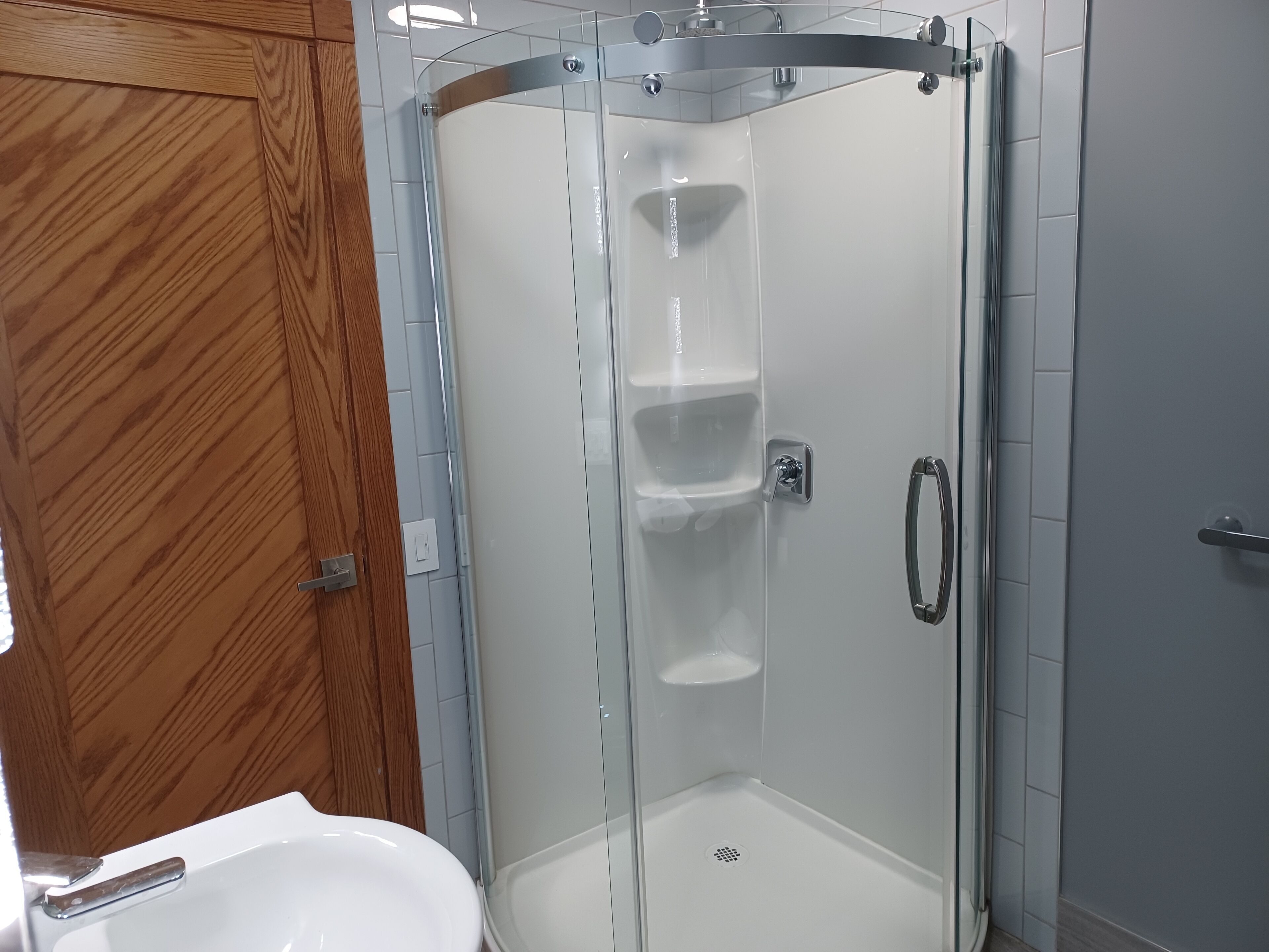 A modern bathroom with a glass-enclosed shower, a wooden door, and a white sink.